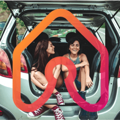 Duas amigas sentadas no bagageiro de um carro e uma logo indicando uma casa sobrepondo a imagem